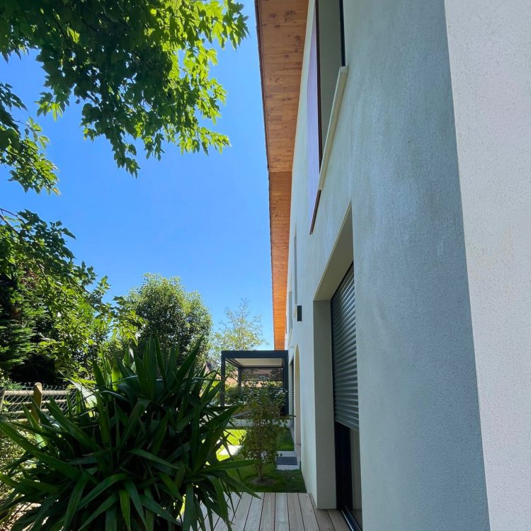 Photographie lointaine de la pergola intégrée à l'aménagement extérieur de la ville neuve, soulignant son design fonctionnel et élégant.